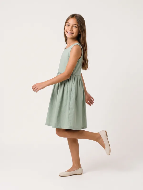 Menina de perfil com o vestido verde, uma perna erguida para trás